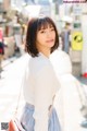 A woman in a white sweater and blue skirt is walking down the street.