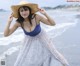 A woman in a blue dress and a straw hat on the beach.