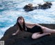 A woman in a black bathing suit laying on a rock by the ocean.