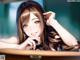 Anime girl with long brown hair and blue eyes sitting at a table.